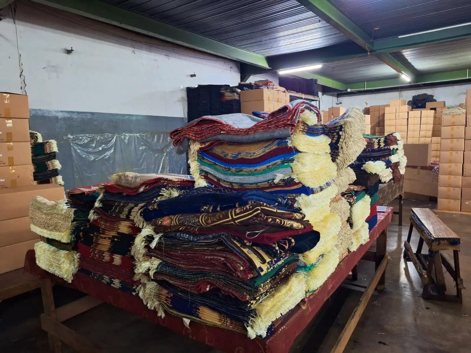 Stacks of finished premium chenille prayer rugs and packaged boxes in the Sakakriya.id warehouse, ready for international wholesale shipment