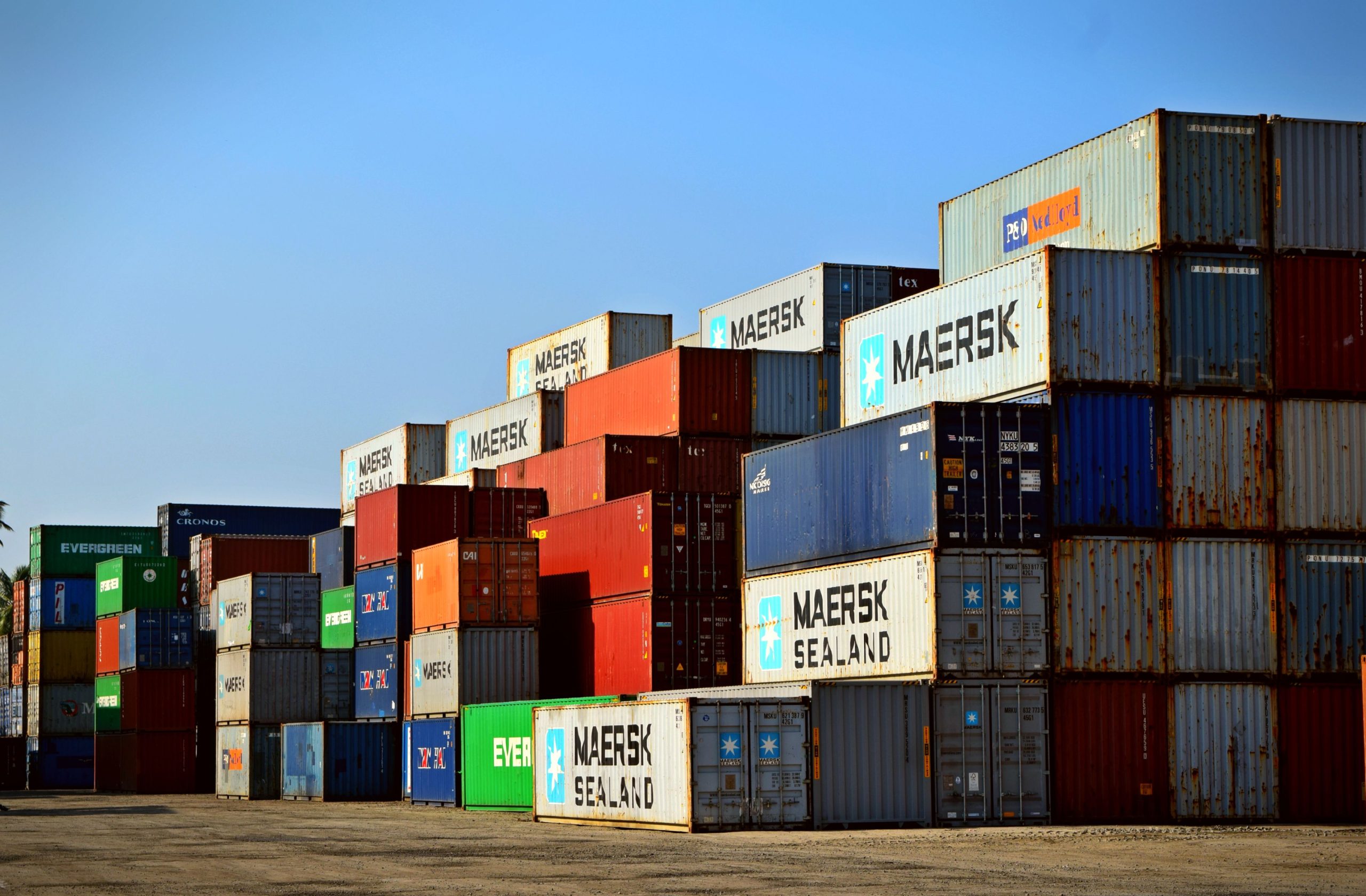 Stacked shipping containers at a port, representing global sourcing and export logistics comparison between Indonesia and China prayer rug manufacturers
