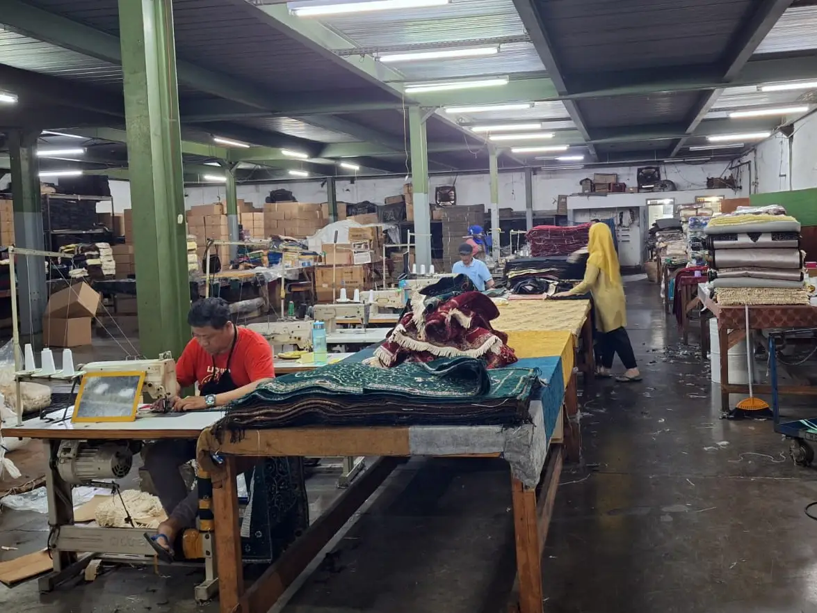 Skilled artisans working at a large-scale textile sewing workshop in Indonesia, producing bulk prayer rugs and carpets for global wholesale distribution